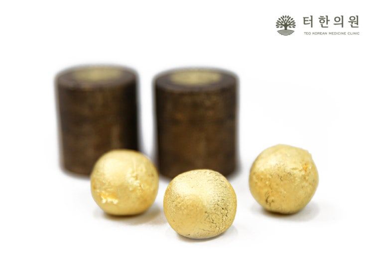 흰 배경에 놓인 금박 한약 환 세 알과 갈색 용기 두 개